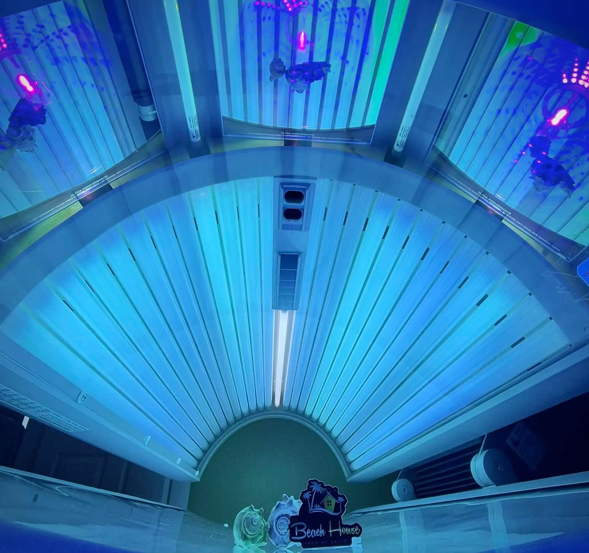 Looking up into a tanning bed lit bright blue, with a Beach House sign at its foot